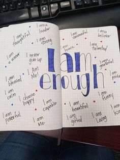 an open notebook with the words i am enough written in blue ink on top of it