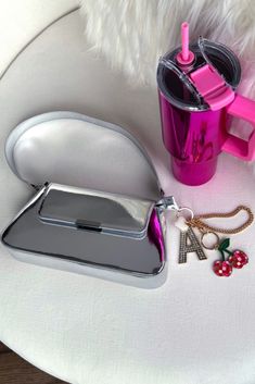 a pink purse and some other items on a white table with a silver coffee cup