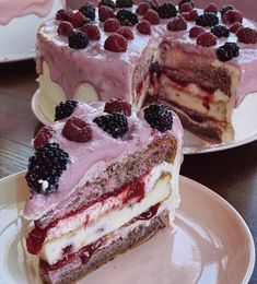 two pieces of cake on plates with raspberries and blackberries in the middle