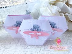 three pink and white boxes with teddy bears on them sitting on a lace tablecloth