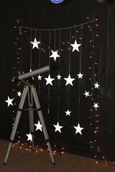 a telescope on a tripod in front of a wall with stars hanging from it