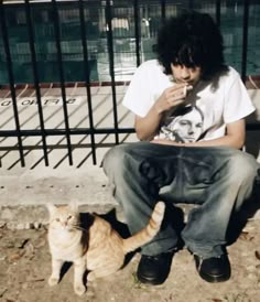 a man sitting on a bench next to a cat and eating something out of his hand