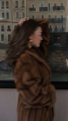 a woman in a fur coat is walking by a wall with a painting behind her