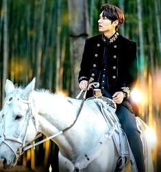 a woman riding on the back of a white horse in front of bamboo tree's