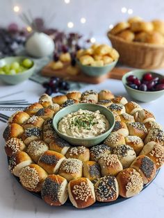 a platter filled with rolls and dip surrounded by other food items on a table