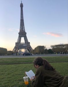 a woman sitting in front of the eiffel tower reading a book