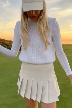 a woman in a white tennis outfit and hat is holding her hands out to the side