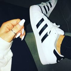 a woman's hand with white nail polish and adidas sneakers