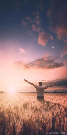 a man standing in a wheat field with his arms spread out and the sun setting behind him