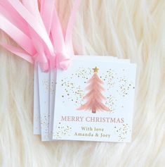 a christmas card with pink ribbon and gold glitters on it next to a white fur background