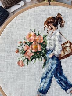 a cross stitched picture of a woman carrying flowers