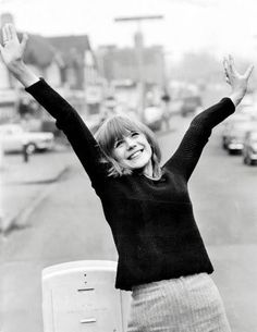 a woman standing on the side of a road with her arms in the air