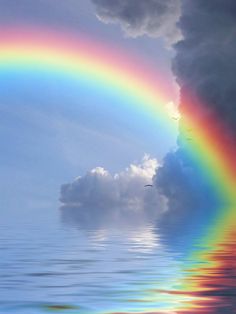 a rainbow in the sky over water with clouds