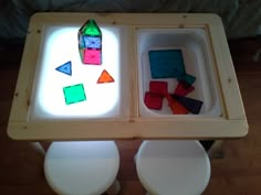 two white toilets sitting next to each other on top of a wooden table covered in colored tiles