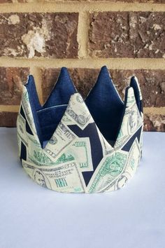 a crown made out of dollar bills sitting on top of a white table next to a brick wall