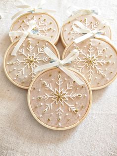 four embroidered snowflake ornaments with ribbon tied around them on a white tablecloth