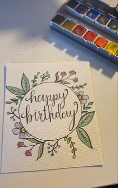 a card with the words happy birthday on it and some watercolor paints next to it