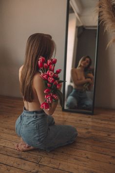 a woman sitting on the floor in front of a mirror with red tulips