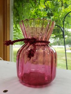 a pink glass vase sitting on top of a table next to a window with trees in the background