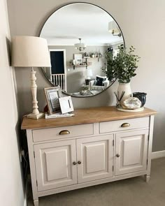 a white dresser topped with a mirror next to a lamp