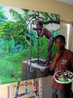 a man standing in front of a painting holding a paintbrush and palette next to it