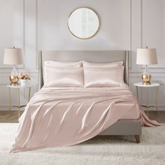 a bed with pink sheets and pillows in a white room next to two nightstands