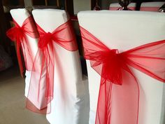 two white chairs with red sashes and bows tied to the back of each chair