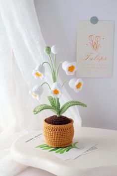 a crochet potted plant with white and yellow flowers in it sitting on top of a table