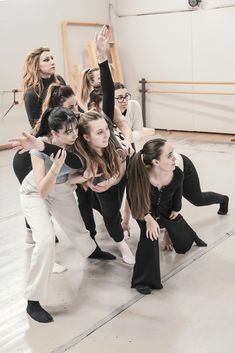 a group of young women standing next to each other in a dance studio with their arms up