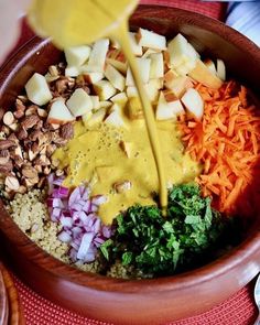 a bowl filled with chopped vegetables and dressing being poured into the mixtures in it