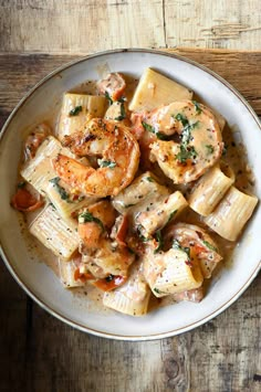 a white bowl filled with pasta and shrimp on top of a wooden table next to a fork