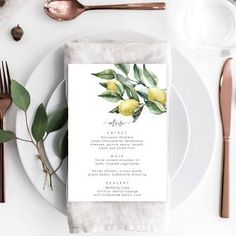 a place setting with white plates and silverware, gold utensils and greenery