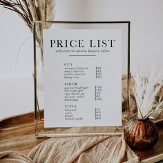 a price list sitting on top of a table next to a vase filled with dry grass