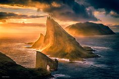 the sun is setting over an island in the ocean with two large rocks sticking out of it