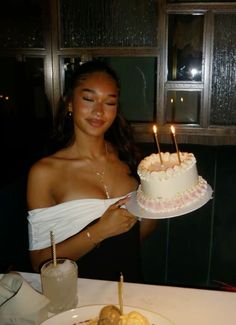 a woman holding a cake with candles on it in front of a plate full of food