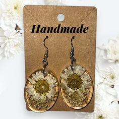 a pair of earrings with flowers on them sitting in front of some white and yellow flowers