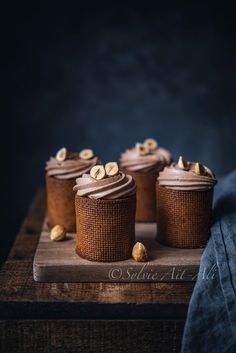 four cupcakes with chocolate frosting and nuts are on a wooden cutting board