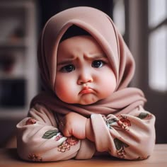 a baby wearing a pink hijab sitting on top of a wooden table