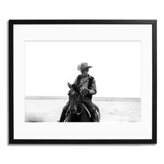 a black and white photo of a man riding a horse in the desert with his hat on