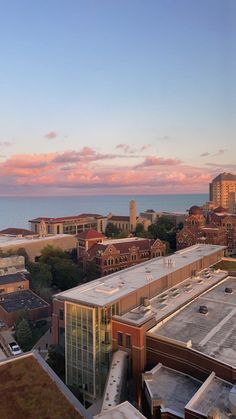 an aerial view of a city with buildings and the ocean in the background at sunset