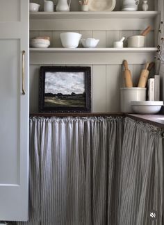 a kitchen with white shelves and dishes on top of it, along with a framed photograph