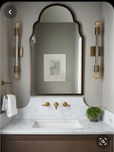 a bathroom vanity with marble counter top and gold faucet, mirror above it