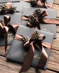 four wrapped gift boxes with pine cones and ribbons tied around them on a wooden table