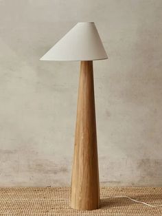 a wooden table lamp with a white shade on the top and bottom, in front of a beige wall