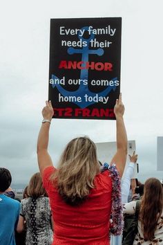 a woman holding up a sign that reads every family needs their anchor and our's comes home today