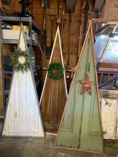 three wooden christmas trees with wreaths on them in a workshop area, one is green and the other is white