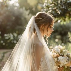 a woman in a wedding dress is holding a bouquet and looking down at her veil