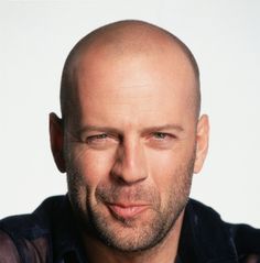 a balding man with a blue shirt and black shirt is looking at the camera