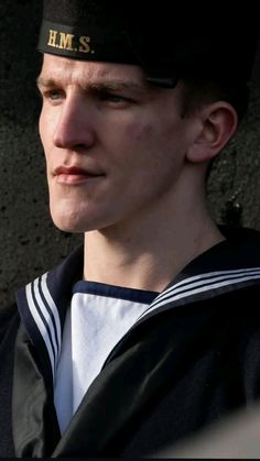 a young man in a sailor's cap looks off into the distance