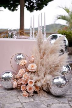 the table is set with silver balls and flowers